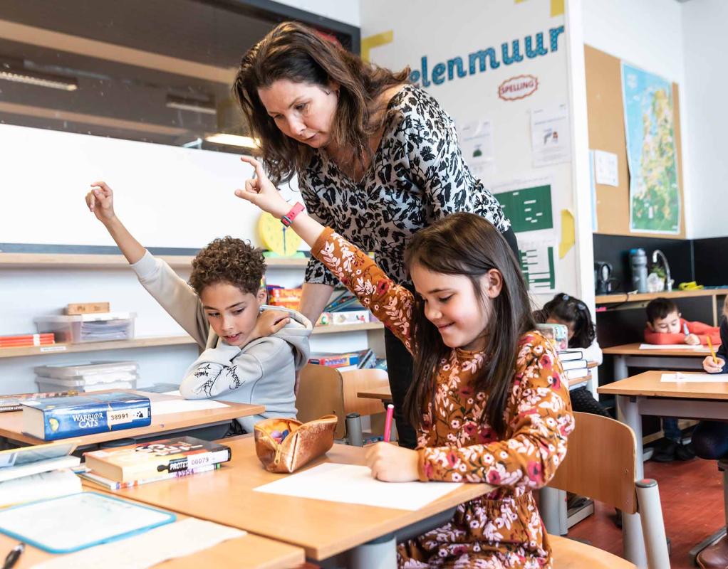 leerkracht helpt leerlingen tijdens schoolopdracht