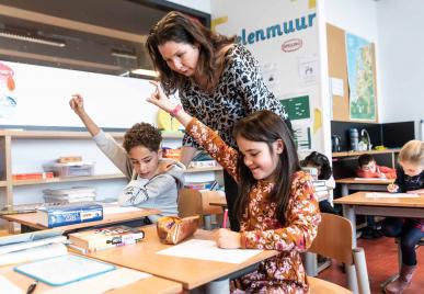 leerkracht helpt leerlingen tijdens schoolopdracht